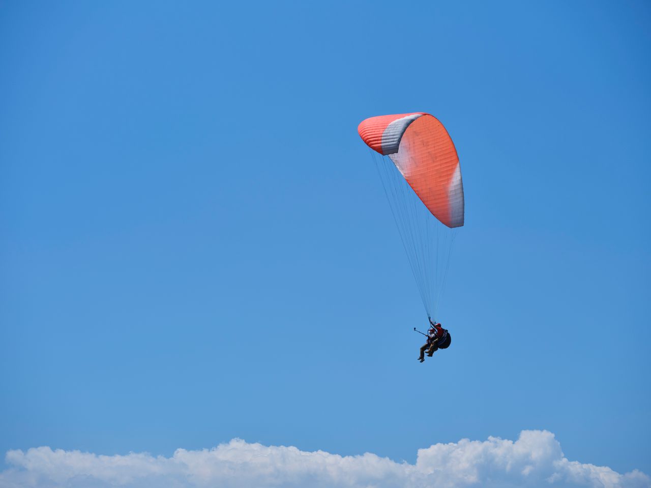 Paraglider soaring gracefully with a vibrant red parachute against a blue sky backdrop.