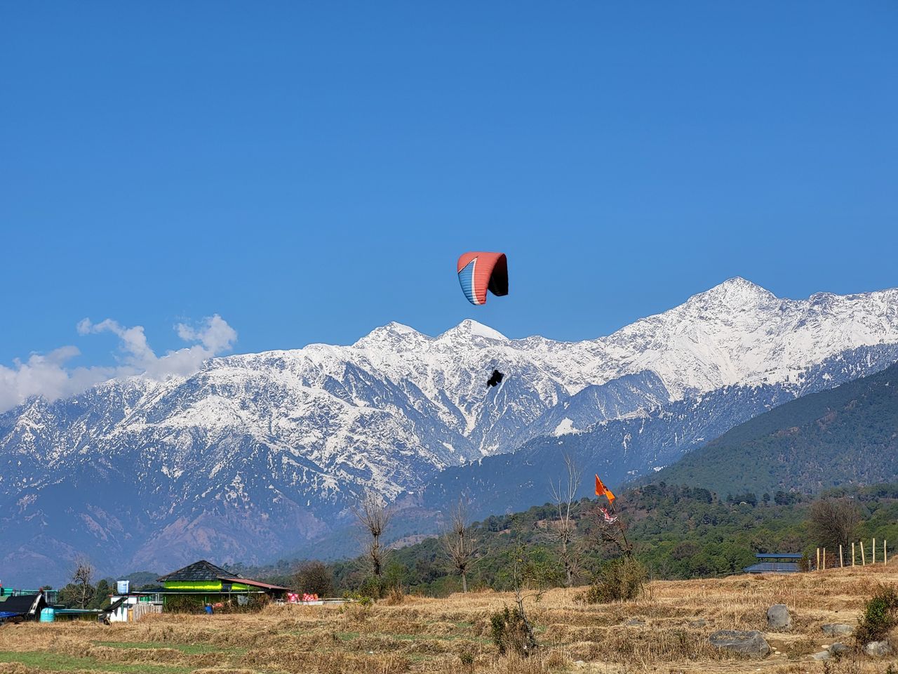 Paragliding adventure over the scenic snowy mountains of Bir, India, under a clear blue sky.