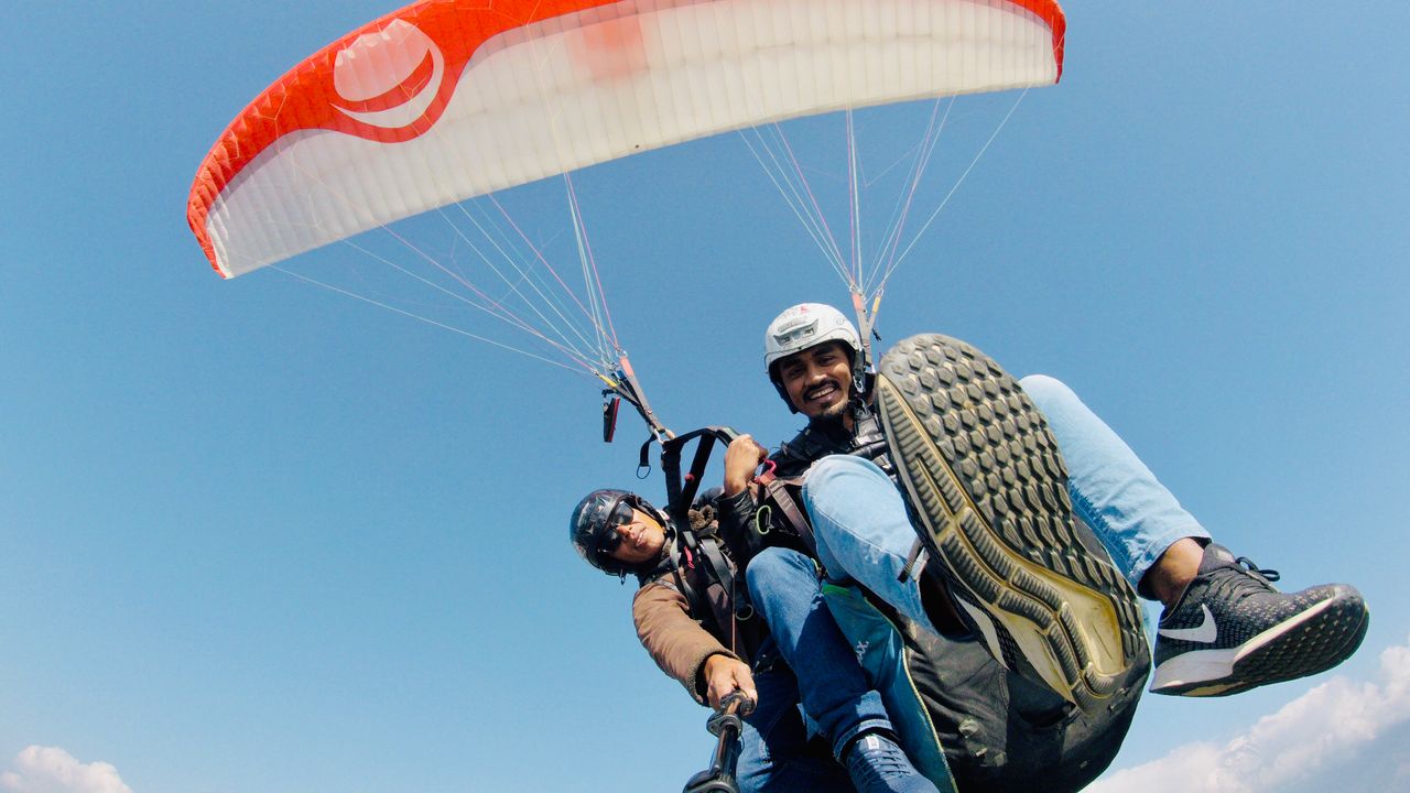 Two men enjoying tandem paragliding against the clear blue sky.